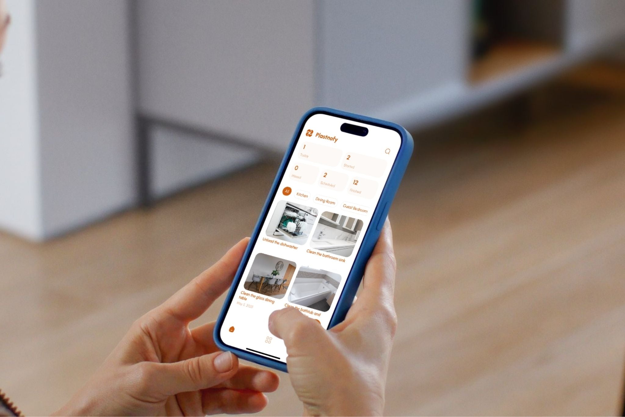 Person holding a smartphone with Plastnofy house cleaning app open on a blurred indoor background