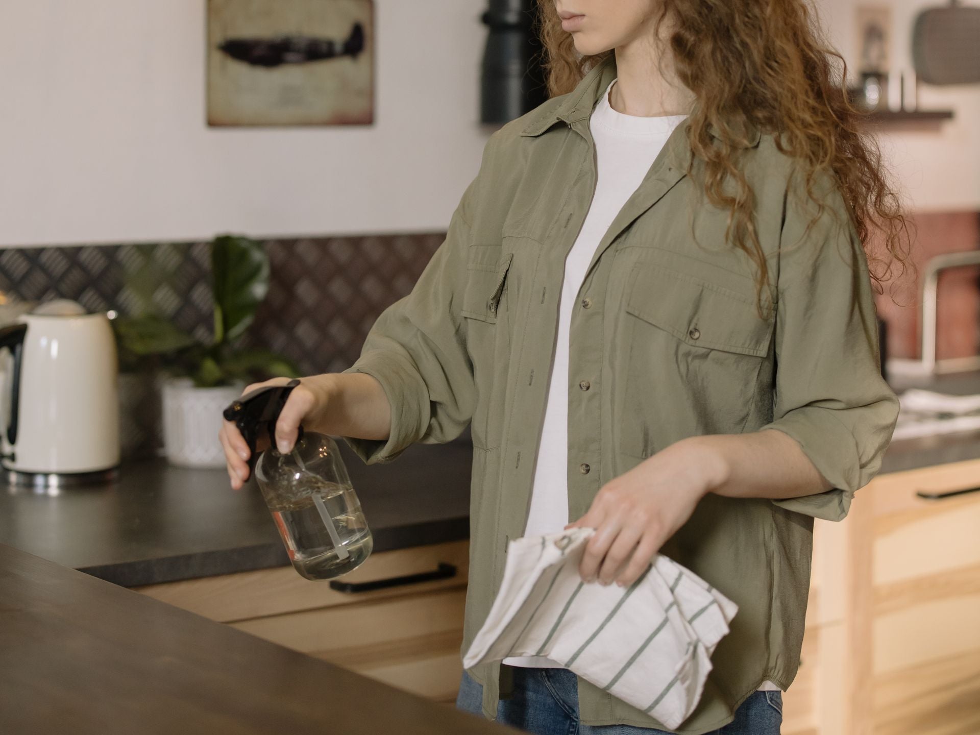 A reusable spray bottle being refilled at home to cut down on single-use plastic cleaner bottles