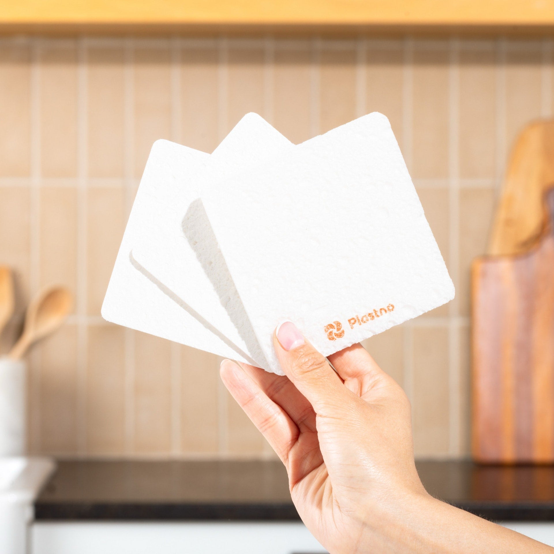 Plastno Soak Sponge: hand holding three square cellulose dish sponges from the 3-pack in a kitchen