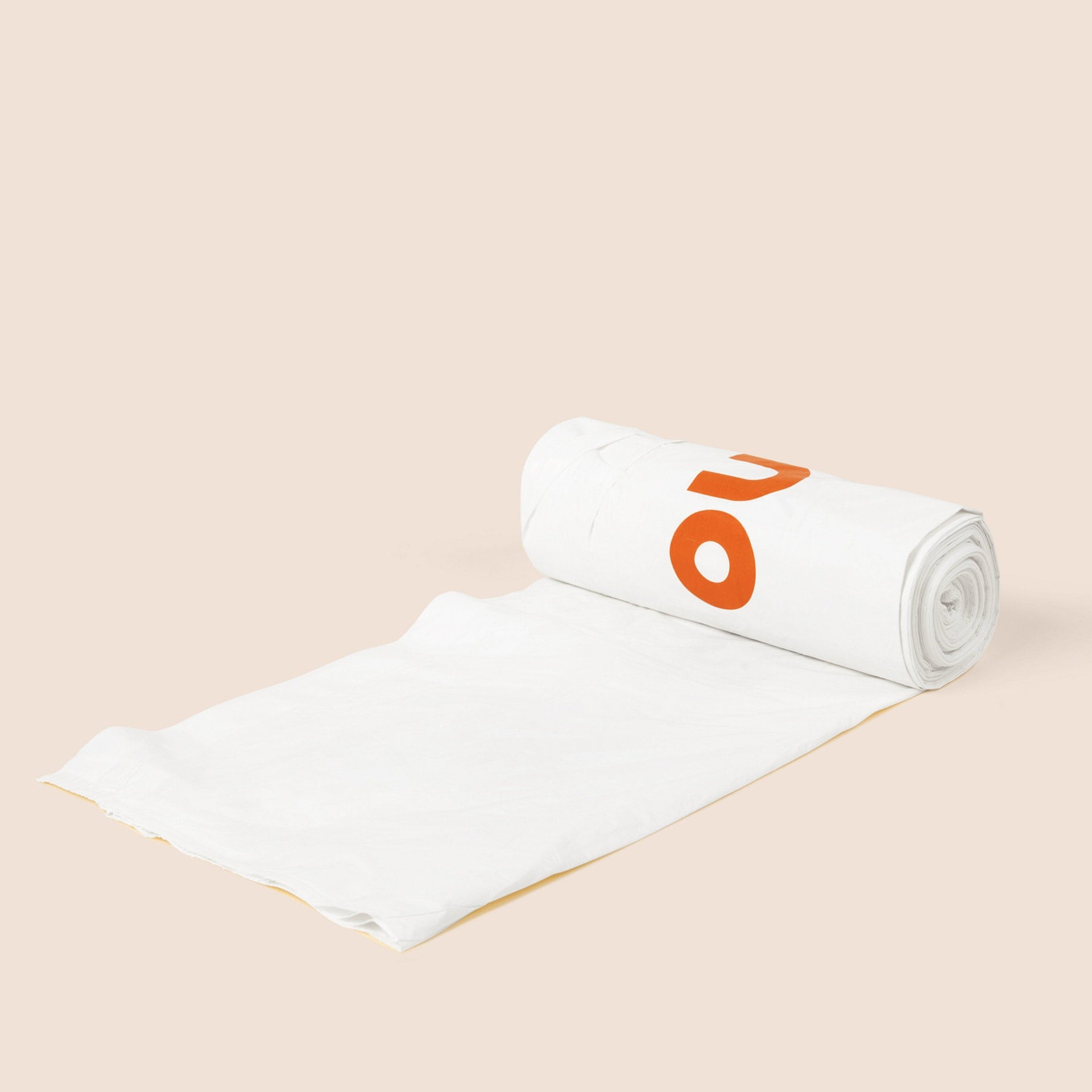 Plastno tall compostable waste bag partially unrolled from its roll, cream-colored with orange Plastno logo