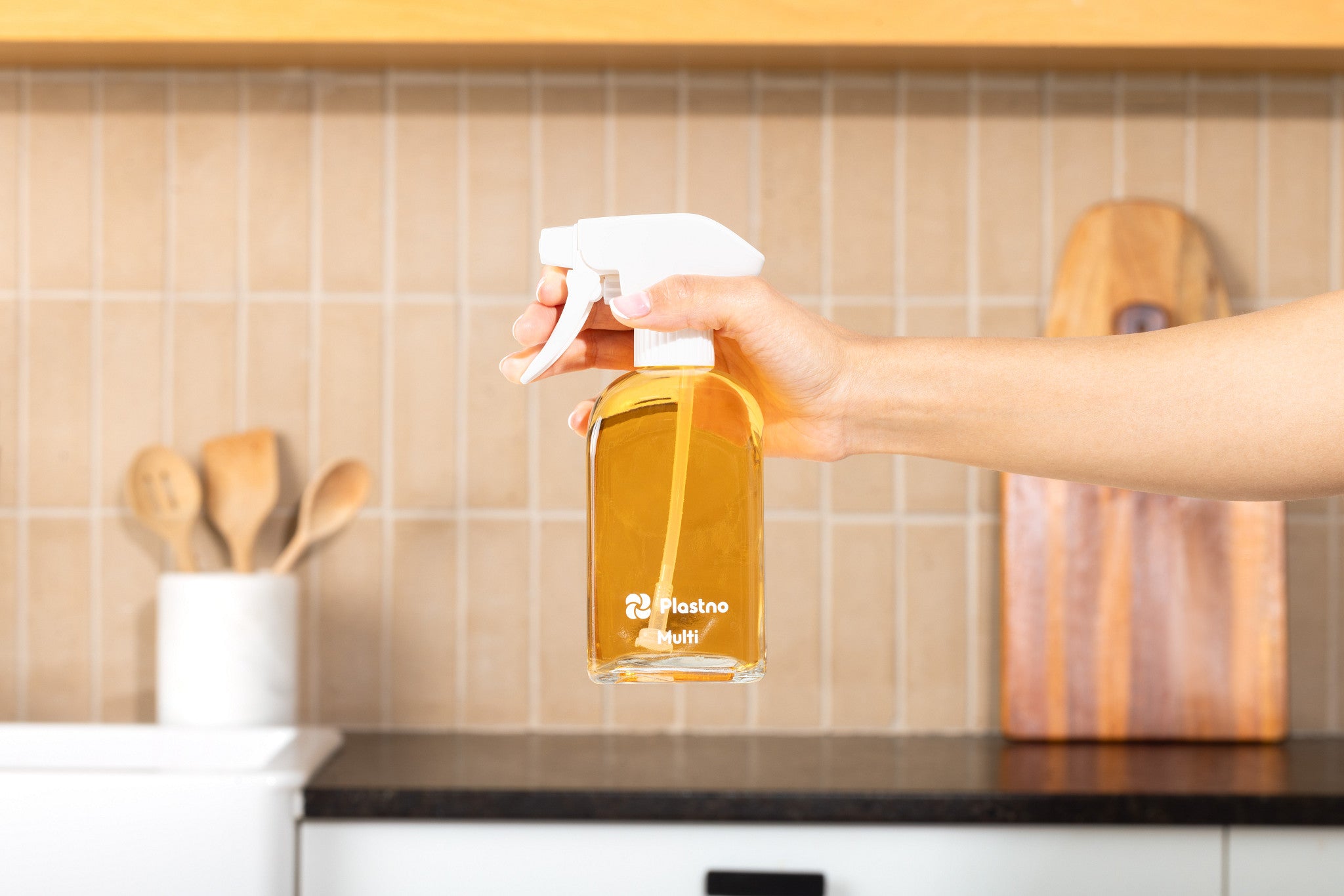 Hand holding the Plastno Multi cleaner glass spray bottle filled with cleaner in a kitchen