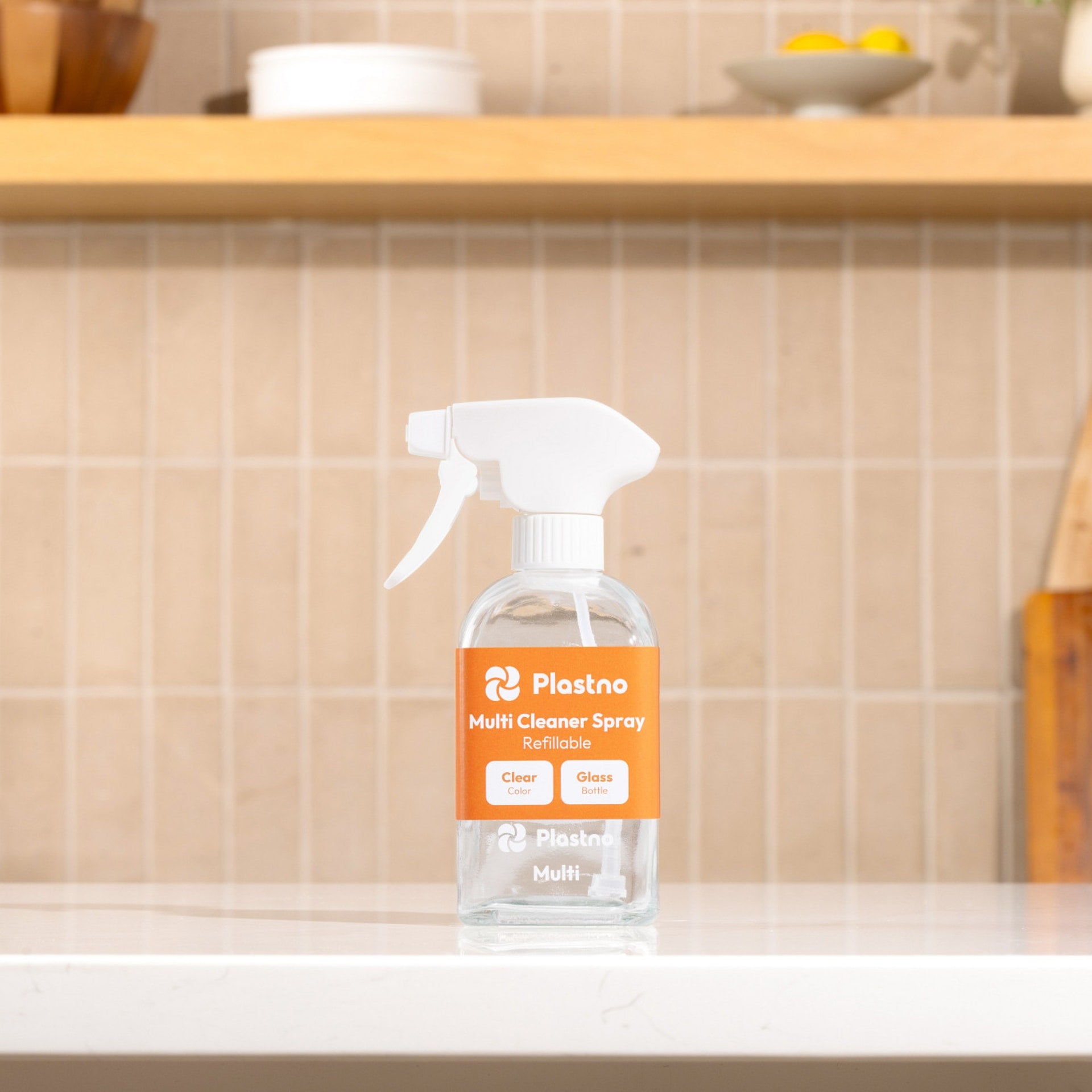Plastno refillable Multi Cleaner Spray glass bottle with orange label on a kitchen counter in front of a tiled backsplash