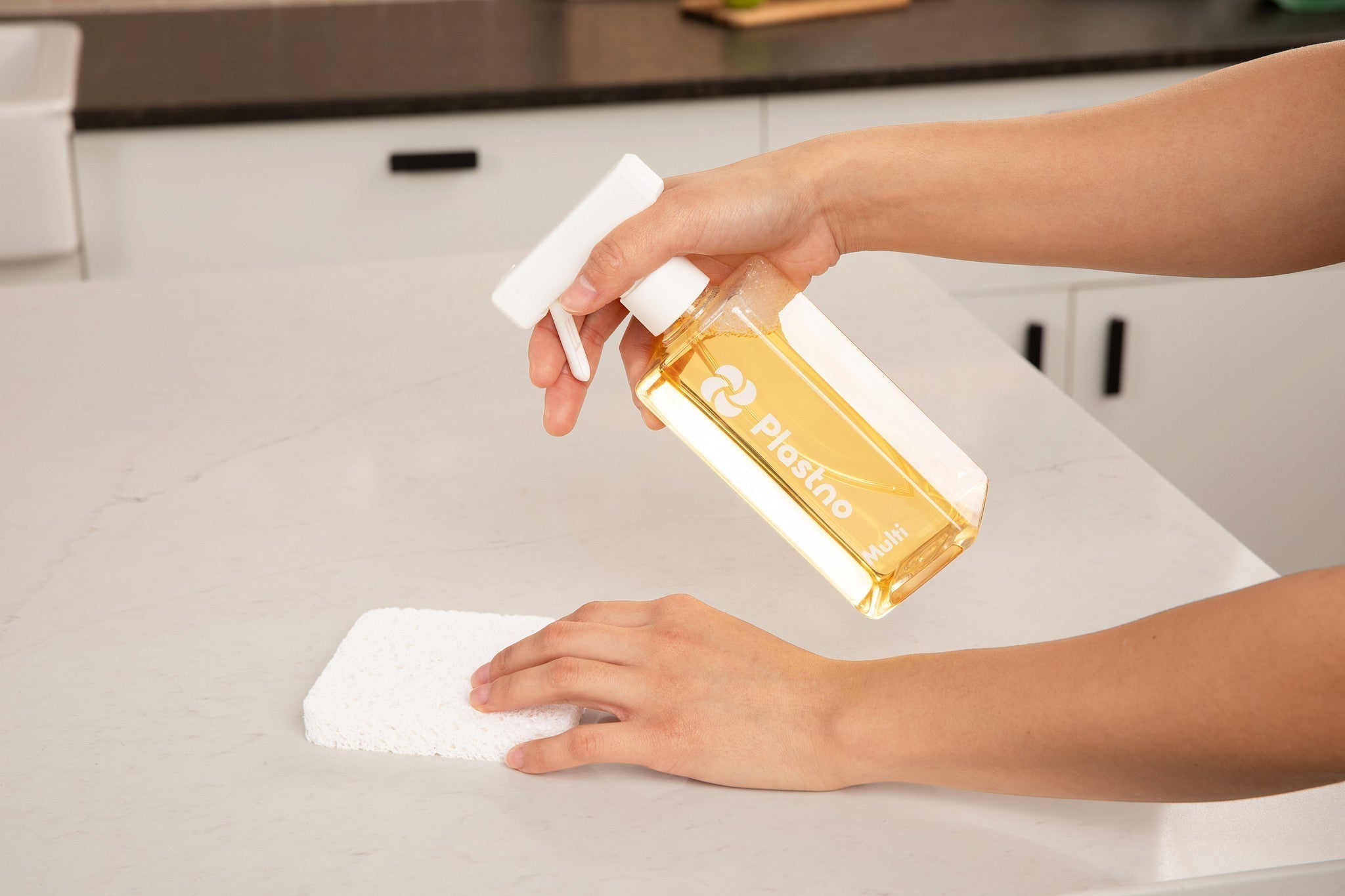 Plastno fragrance-free multi-surface cleaner sprayed on a sealed stone countertop next to a plant-based sponge