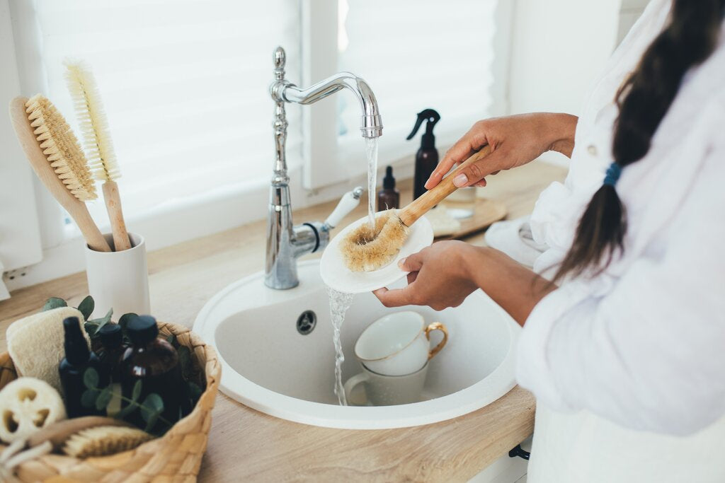 woman washing dishes using wooden brush
