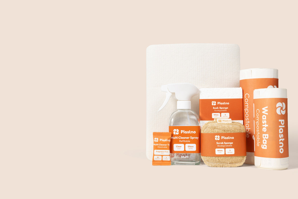 Plastno cleaning bundle: multi cleaner tablet, refillable glass spray bottle, scrub sponge, soak sponge, sponge towel and two rolls of compostable waste bags on a beige background