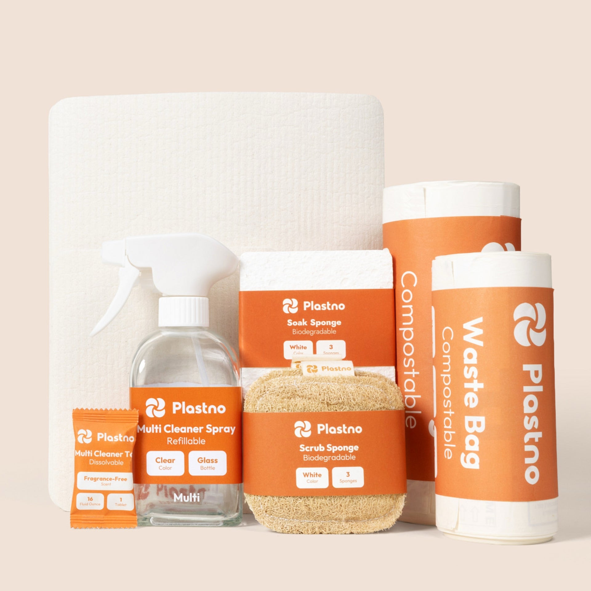 Plastno cleaning bundle: multi cleaner tablet, refillable glass spray bottle, scrub sponge, soak sponge, sponge towel and two rolls of compostable waste bags on a beige background