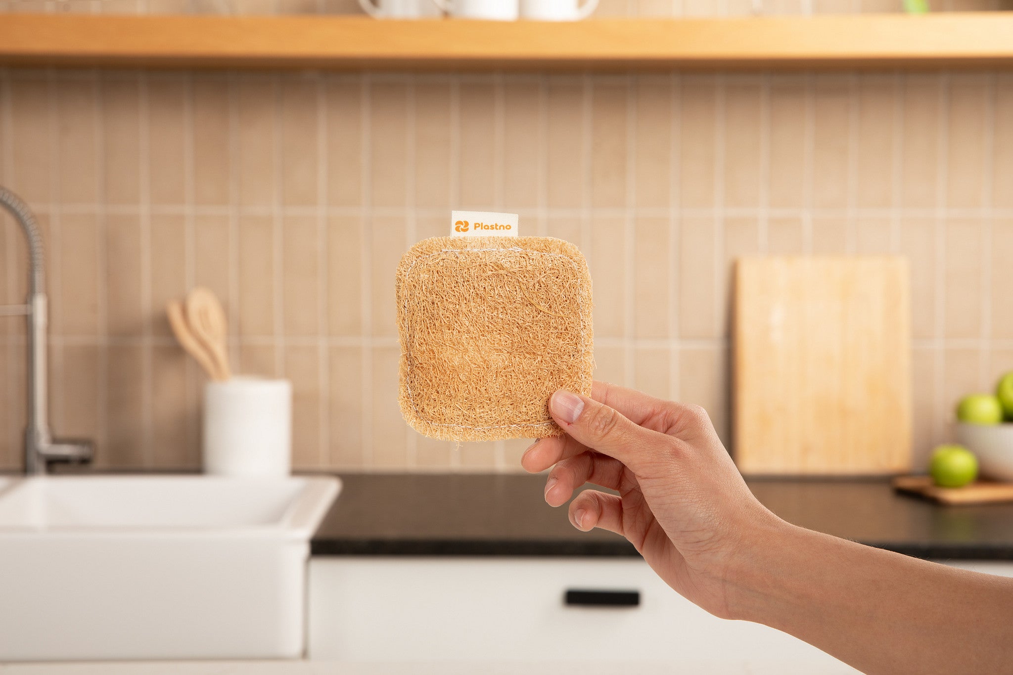 Plastno Scrub Sponge: loofah dish sponge held in front of a tiled kitchen backsplash