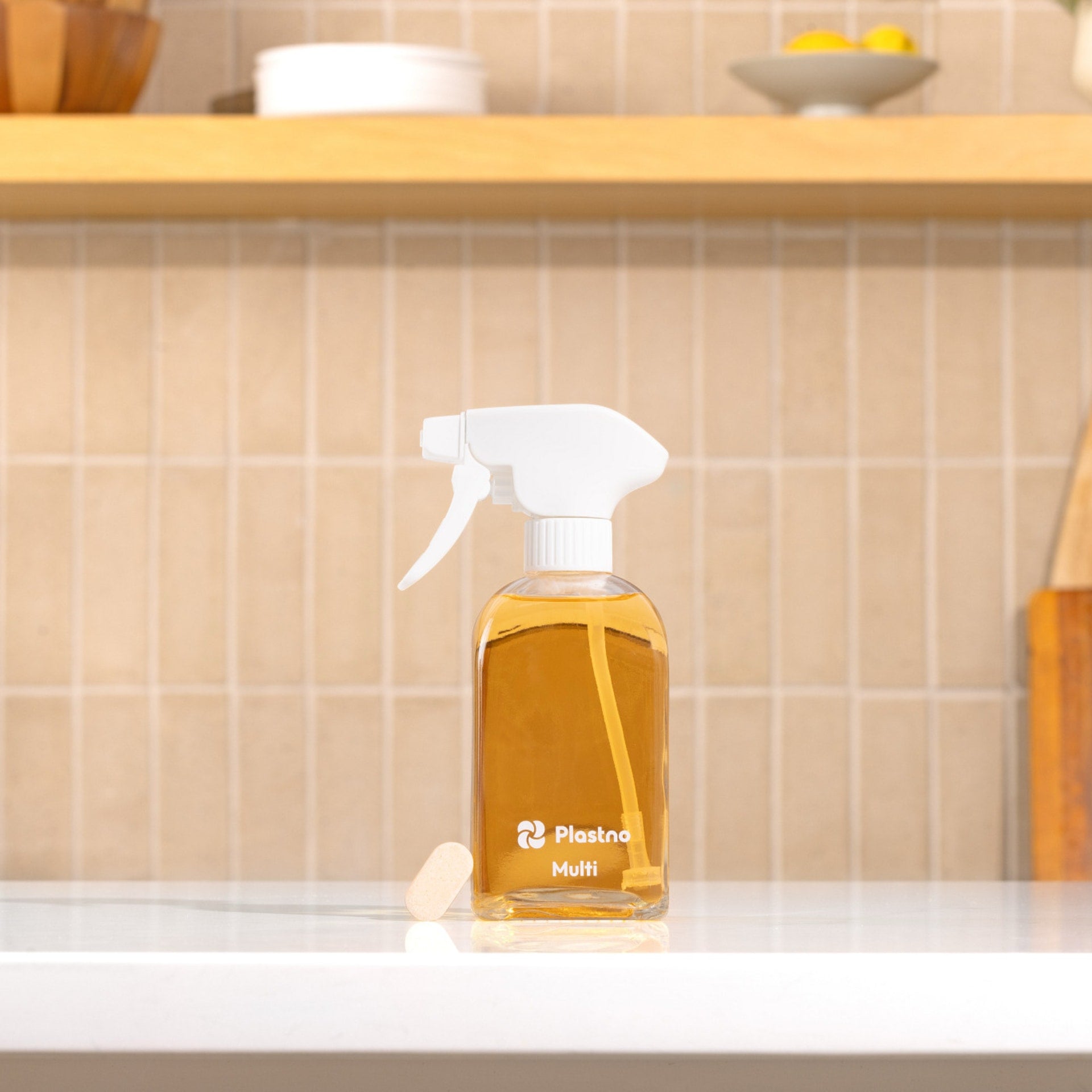 Plastno Multi cleaner glass spray bottle filled with cleaner and a dissolvable tablet on a kitchen counter in front of a tiled backsplash