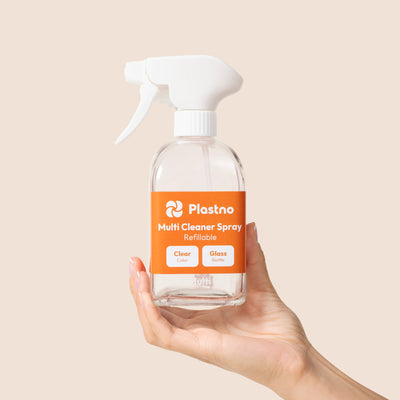 Hand holding the empty Plastno refillable Multi Cleaner Spray glass bottle on a beige background