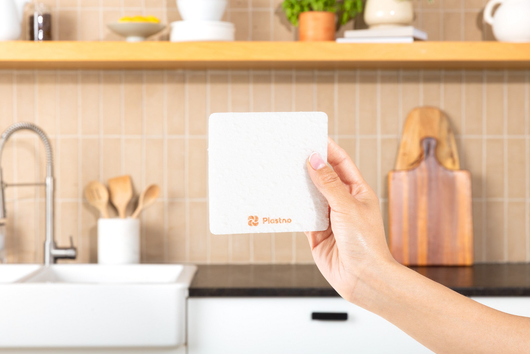 Plastno Soak Sponge: pop-up cellulose dish sponge held in front of a kitchen sink and tiled backsplash
